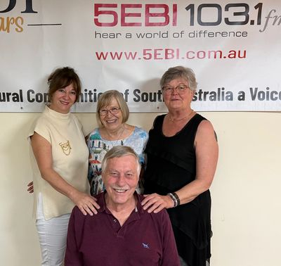 Four smiling adults posing in front of a 5EBI radio station banner.