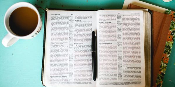 A cup of coffee beside an open Bible on a blue table.
