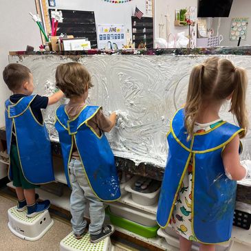 Three children playing with shaving cream on a board.