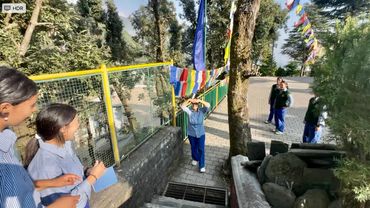 Students in uniforms gather near stairs decorated with colorful flags on a sunny day.