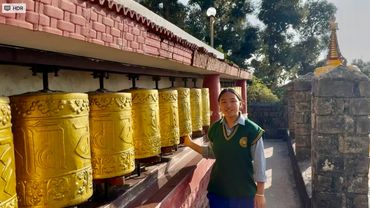 A girl spins golden prayer wheels at a temple under sunlight.