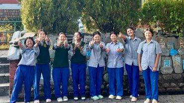 Group of students in blue uniforms giving thumbs up in front of a temple.