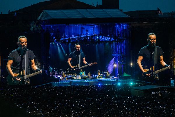 Wide angle shot of Bruce Springsteen playing his guitar and singing into a mic on stage in Rome.