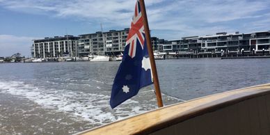 Australian flag waving on a boat near waterfront buildings.