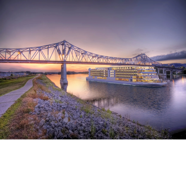 A large cruise ship passes under a steel bridge at sunset on a calm river.