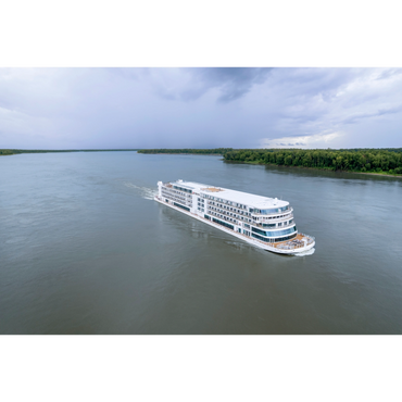 A large white river cruise ship sails on a wide river under a cloudy sky.
