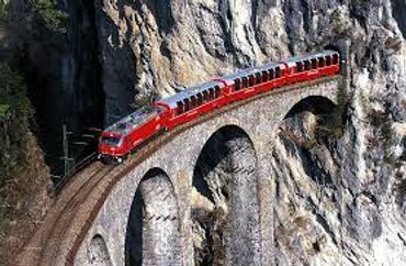 Red train crossing a stone arch bridge on a mountain.