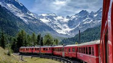Red train winding through snowy mountain landscape under a partly cloudy sky.