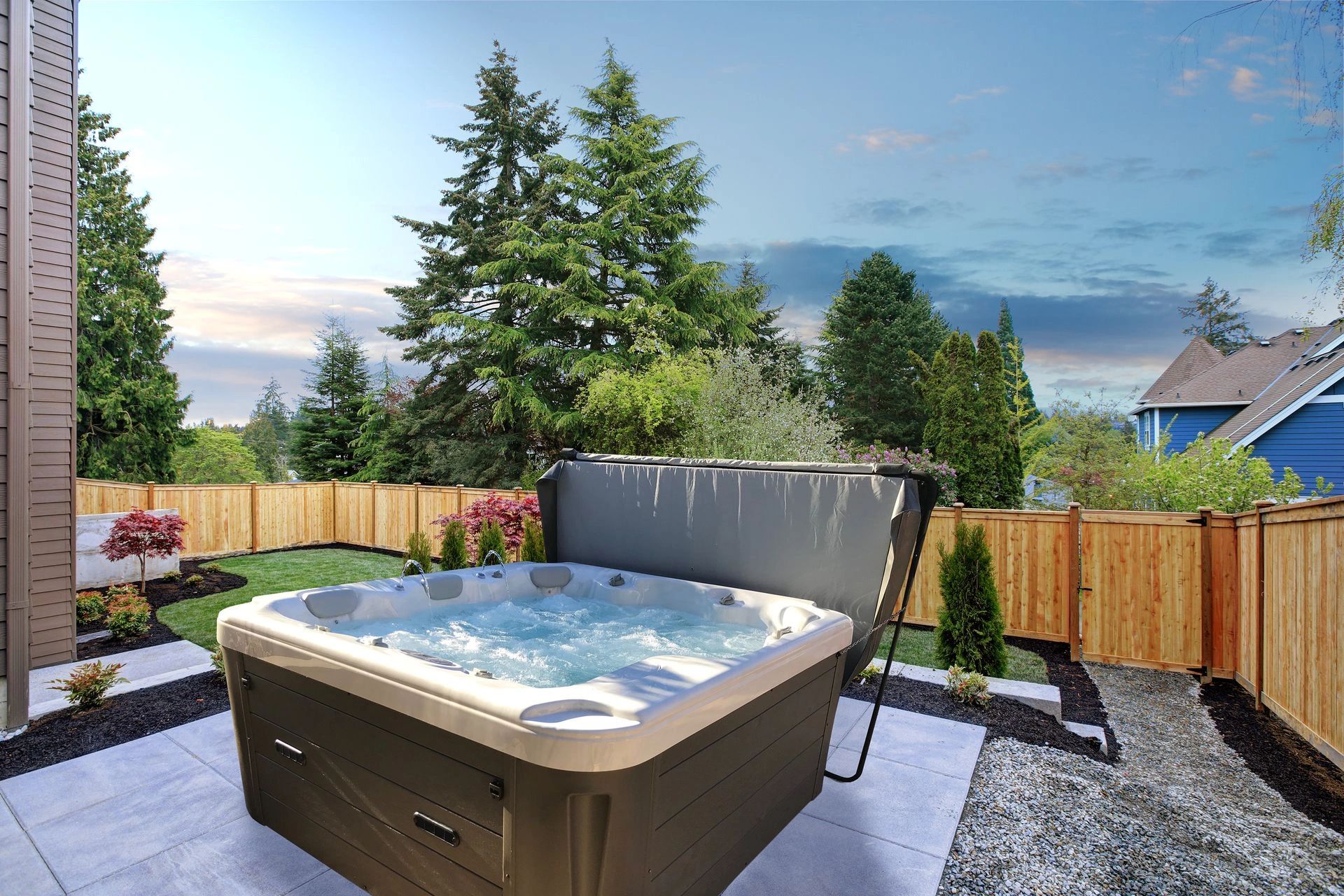 Outdoor hot tub bubbling in a backyard surrounded by trees and a wooden fence.