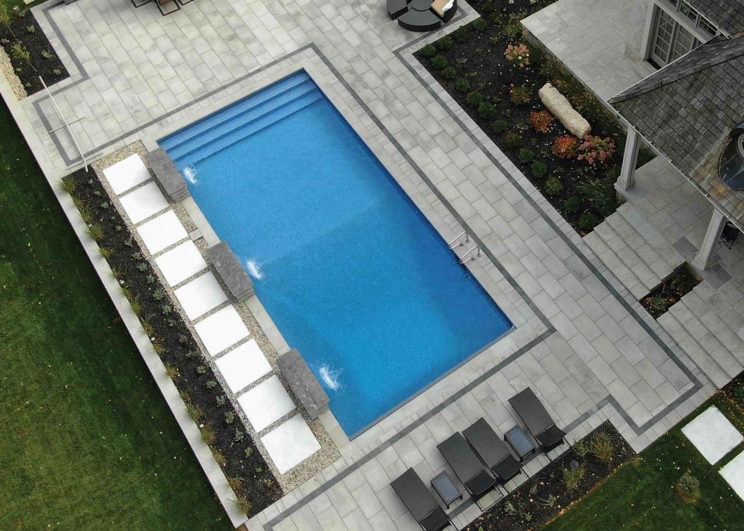 A modern rectangular swimming pool with water features and lounge chairs.
