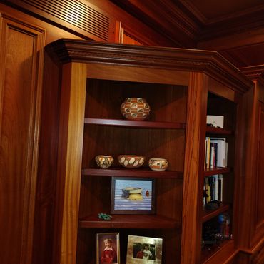 Wooden bookshelf with pottery, paintings, and framed photos.
