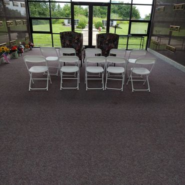 Indoor memorial seating area with folding chairs and floral armchairs.