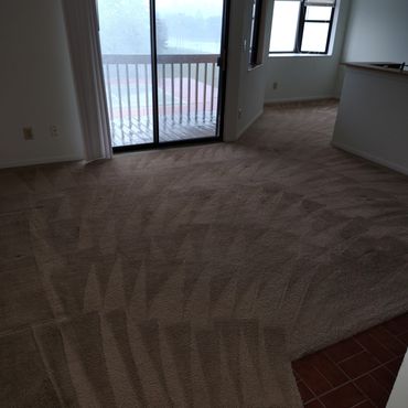 Clean carpeted room with sliding glass door and balcony view on a rainy day.