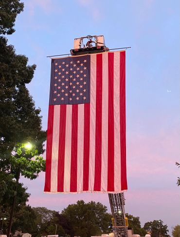 Large American flag hanging from a crane at dusk.