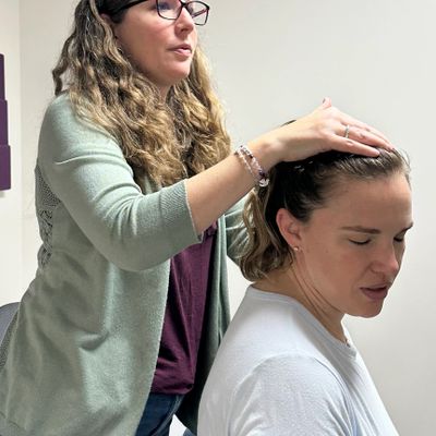 A woman gives a head massage to another woman in a calm setting.