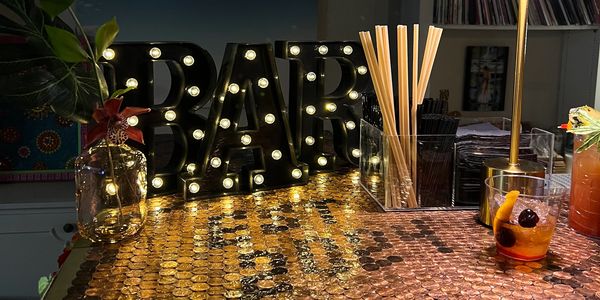 Illuminated bar sign on a penny-covered counter with tropical decor and drinks.