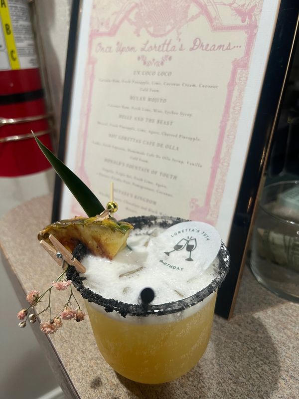 A tropical cocktail garnished with pineapple and a decorative disc for Loretta's 70th birthday.