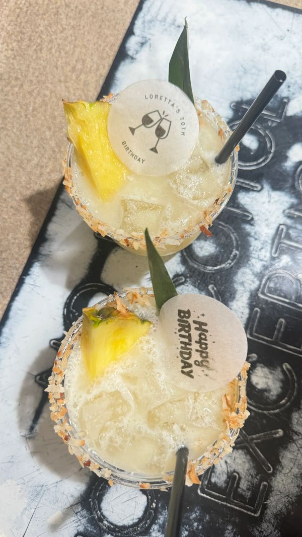 Two tropical birthday cocktails garnished with pineapple and celebratory tags.