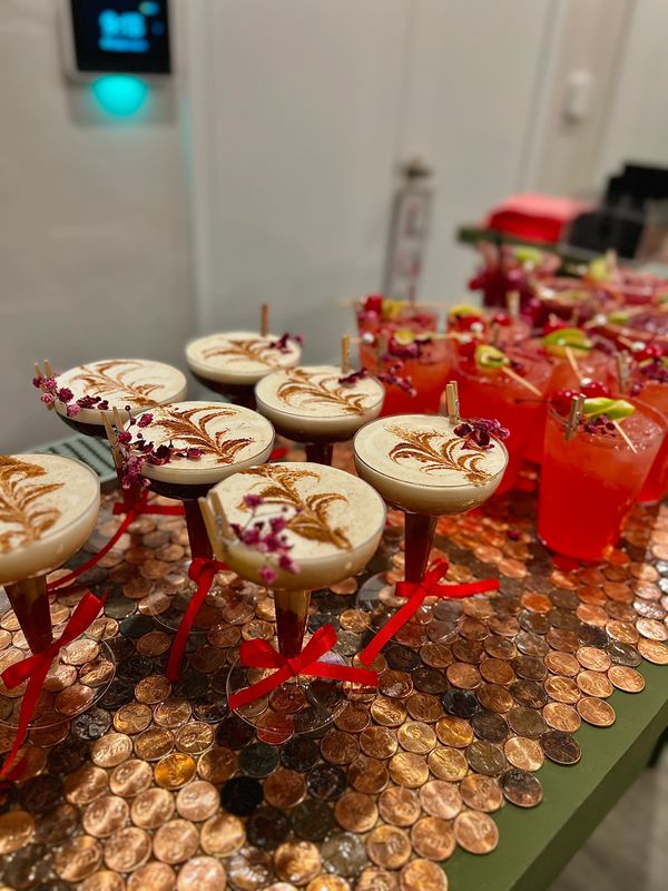 Elegant cocktails with floral garnish and red ribbons on a penny-covered surface.