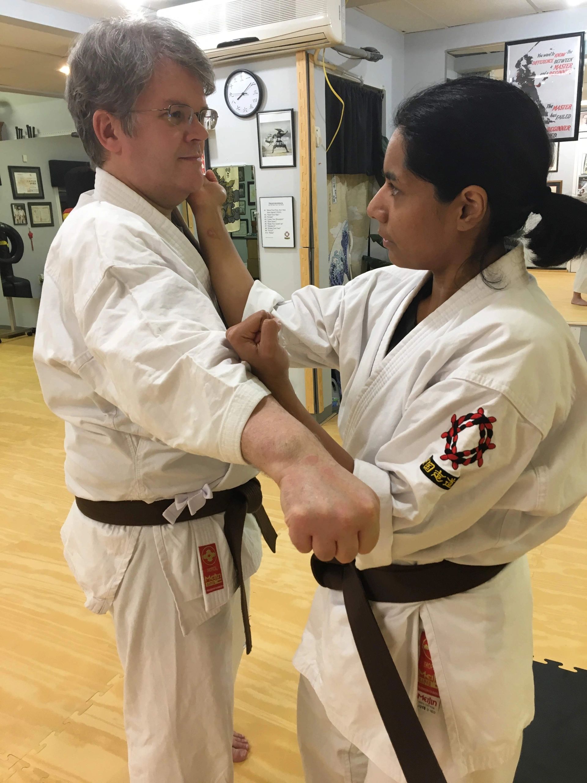 Two martial artists practicing a technique indoors.