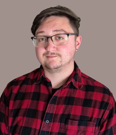 Young man wearing glasses and a red plaid shirt against a plain background.