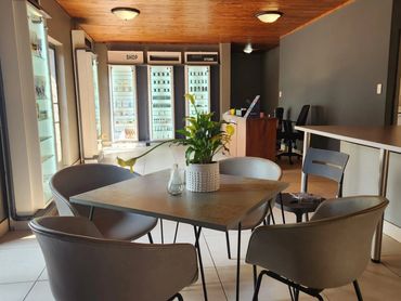 Modern, cozy interior with a table, chairs, and a plant centerpiece near a shop display.