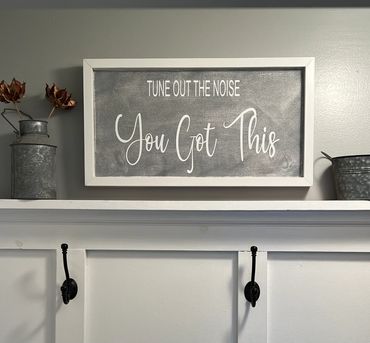 Framed motivational sign saying "Tune out the noise, You Got This" on a shelf.