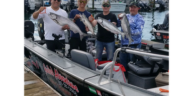 Four men proudly hold large fish on a fishing boat at the dock.