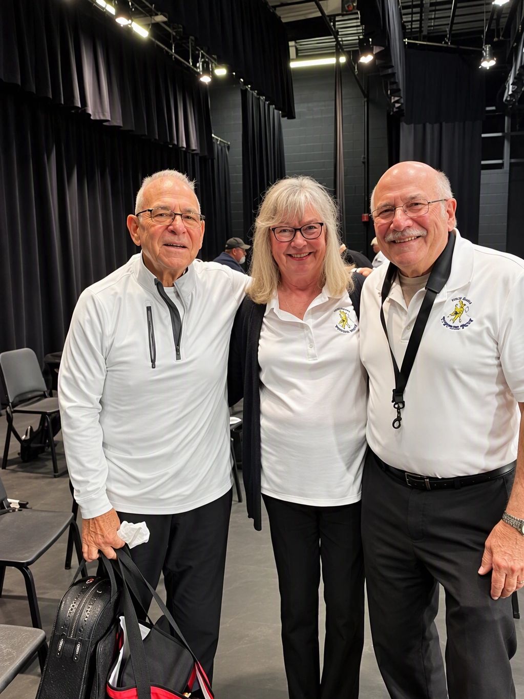 Three smiling older adults in white shirts posing indoors.