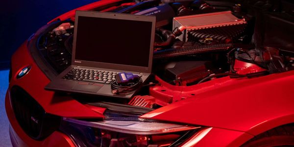 Laptop on a red car's engine compartment under hood.