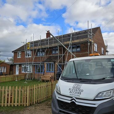 Scaffolding set up around a two-story brick house with a white Elevated Access van in front.