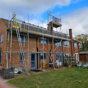 Brick house with blue-trimmed windows surrounded by scaffolding under a cloudy sky.