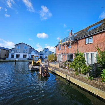 Waterfront houses with scaffolding and construction equipment under a clear blue sky.