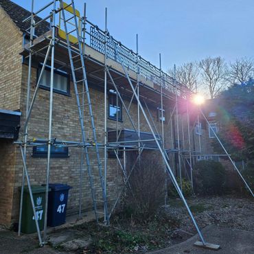 Scaffolding set up around a brick house during sunset.