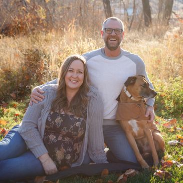 Happy couple sitting outdoors with their dog on a sunny autumn day.