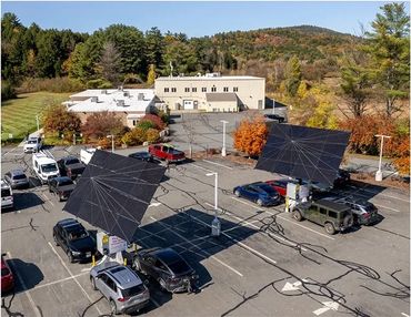 Solar panels installed in a parking lot with cars and surrounding autumn trees.