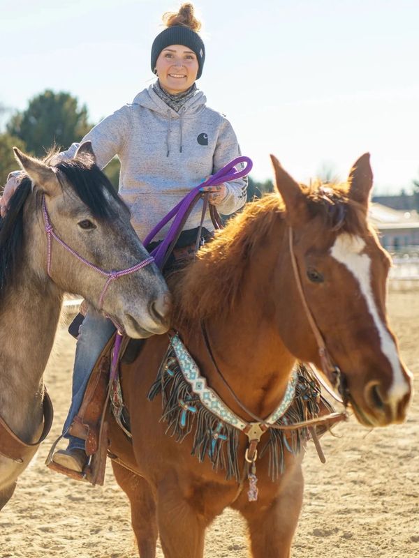 Smiling young woman riding two horses outdoors.