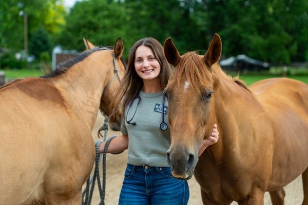 Smiling woman with two horses in an outdoor setting.