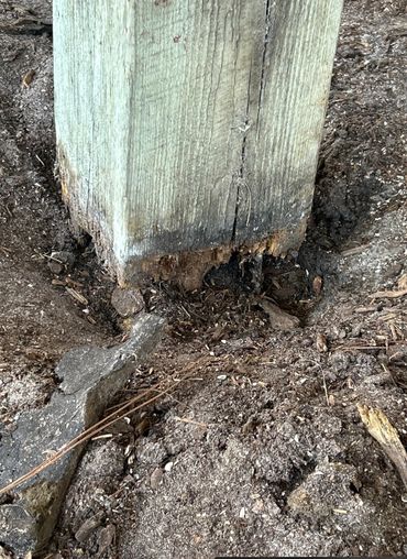 Wood post with visible rot and decay at the base in soil.