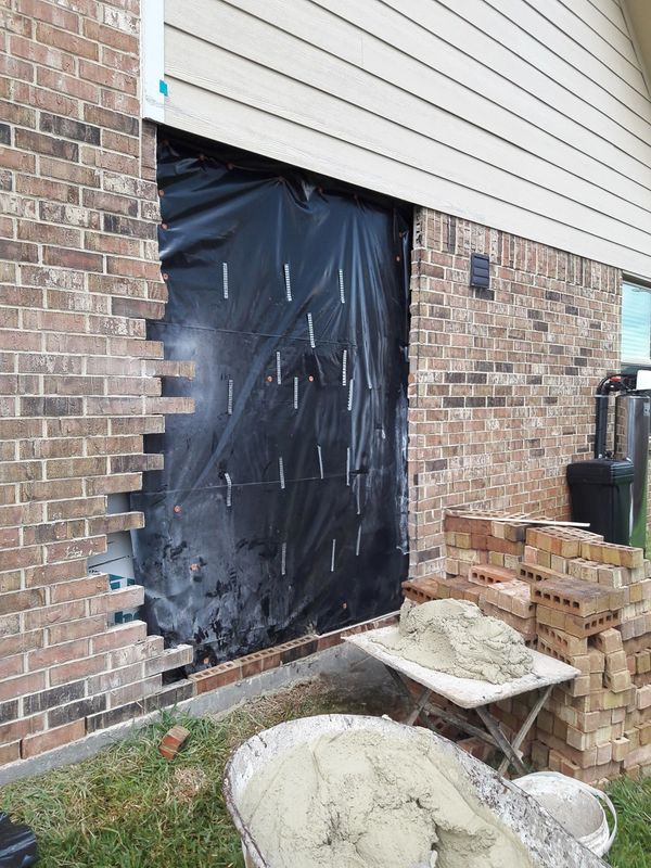 Brick wall with part of the brick removed and a stack of bricks to the side along with some mortar.