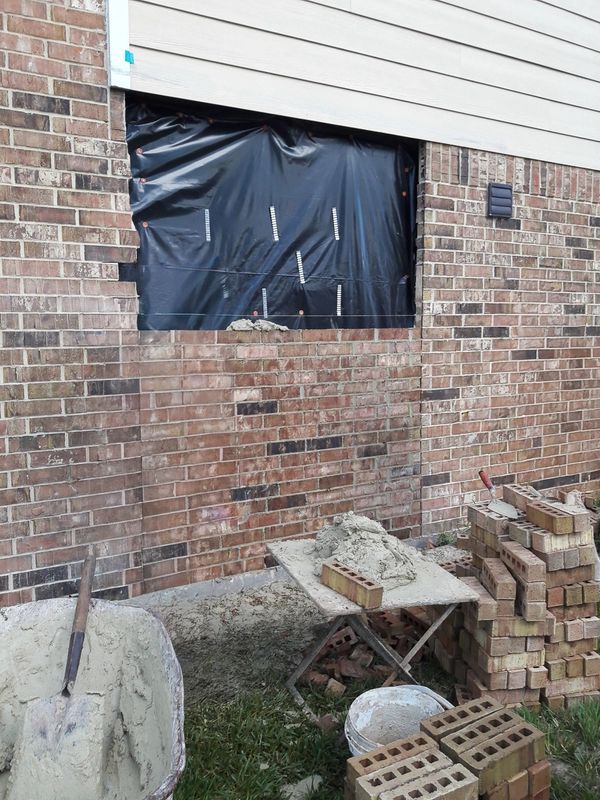 Brick wall with a brick section removed and being reinstalled, half way up.