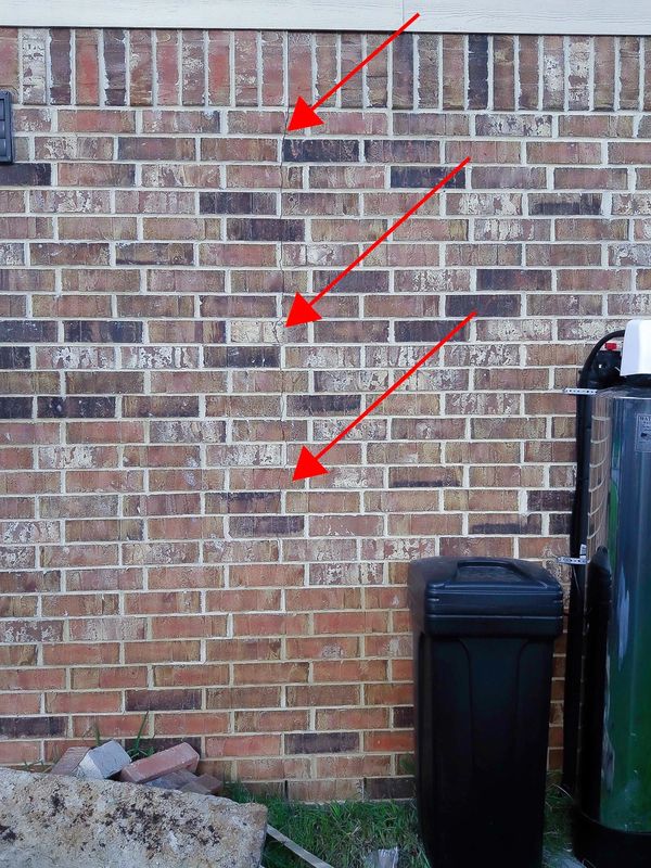 Brick wall with hairline cracks, highlighted with red arroes.