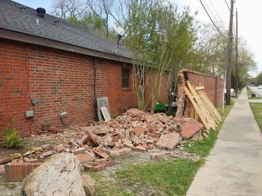 Brick wall at the rear of a house which has fallen, there is a pile of rubble next to it.