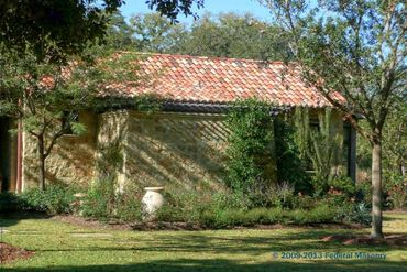 The side of a stone house, stone has different shades of brown, sitting behind a calm tree.