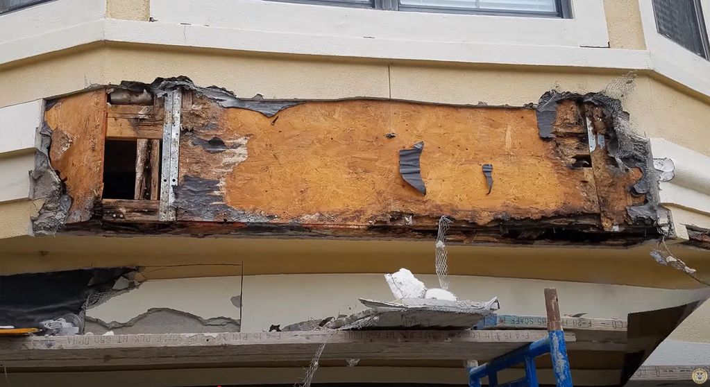 A torn down stucco wall revealing rotten wood and structure.