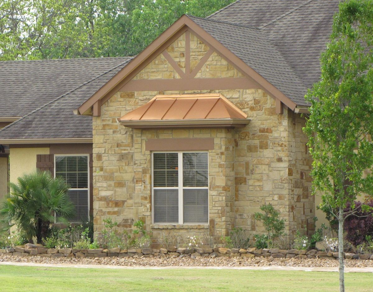 Part of a house with a stone fachade in multiple shades of brown, fully landscaped.