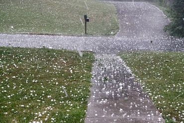 A suburban street and sidewalk covered in hailstones during a storm.