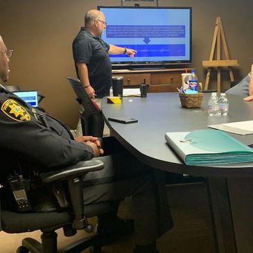 A man presenting information on a screen to a group in a meeting room.