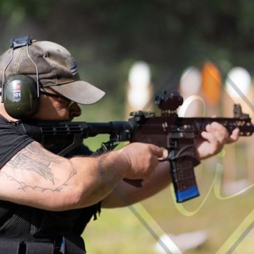 Person aiming a rifle at a shooting range wearing protective gear.