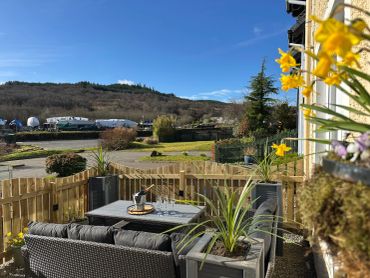 Cozy outdoor patio with wicker furniture, champagne, and flowers under a clear blue sky.
